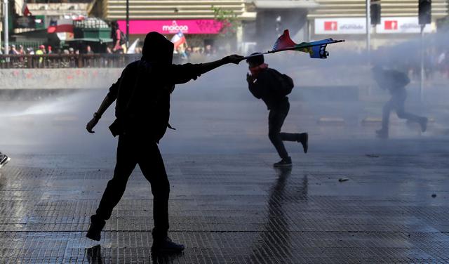 Un manifestante ondea una bandera mapuche mientras la policía antidisturbios rocía agua durante una protesta contra el gobierno en Santiago. (REUTERS / Edgard Garrido).