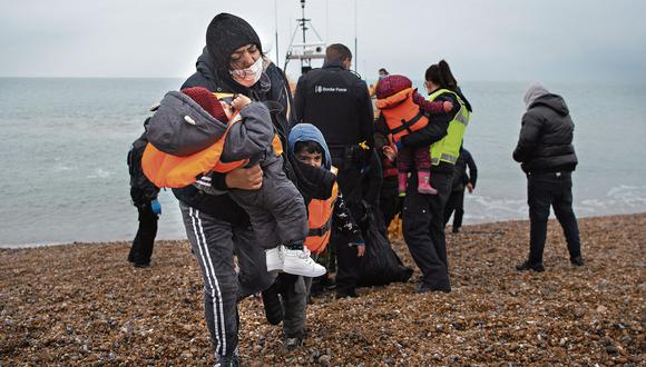 Una migrante carga a sus hijos después de ser ayudada a desembarcar desde un bote salvavidas de la RNLI (Royal National Lifeboat Institution) en una playa de Dungeness, en la costa sureste de Inglaterra (BEN STANSALL / AFP)