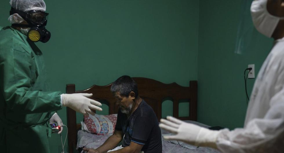Plinio dos Santos, de 65 años y que tenía problemas para respirar, se sienta en su cama mientras el sanitario Wanden Nascimento (izquierda) comprueba su saturación de oxígeno antes de trasladarlo a un hospital, en Manaos, Brasil, el 20 de mayo de 2020. Dos Santos fue admitido en el hospital bajo la sospecha de que padecía COVID-19. (AP Foto/Felipe Dana).