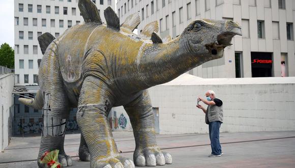 Un hombre toma una fotografía de una gran estatua de un dinosaurio el 25 de mayo de 2021 en Santa Coloma de Gramenet, cerca de Barcelona, ​​donde un hombre de 40 años murió al quedar atrapado dentro de la estatua. (Foto de LLUIS GENE / AFP).
