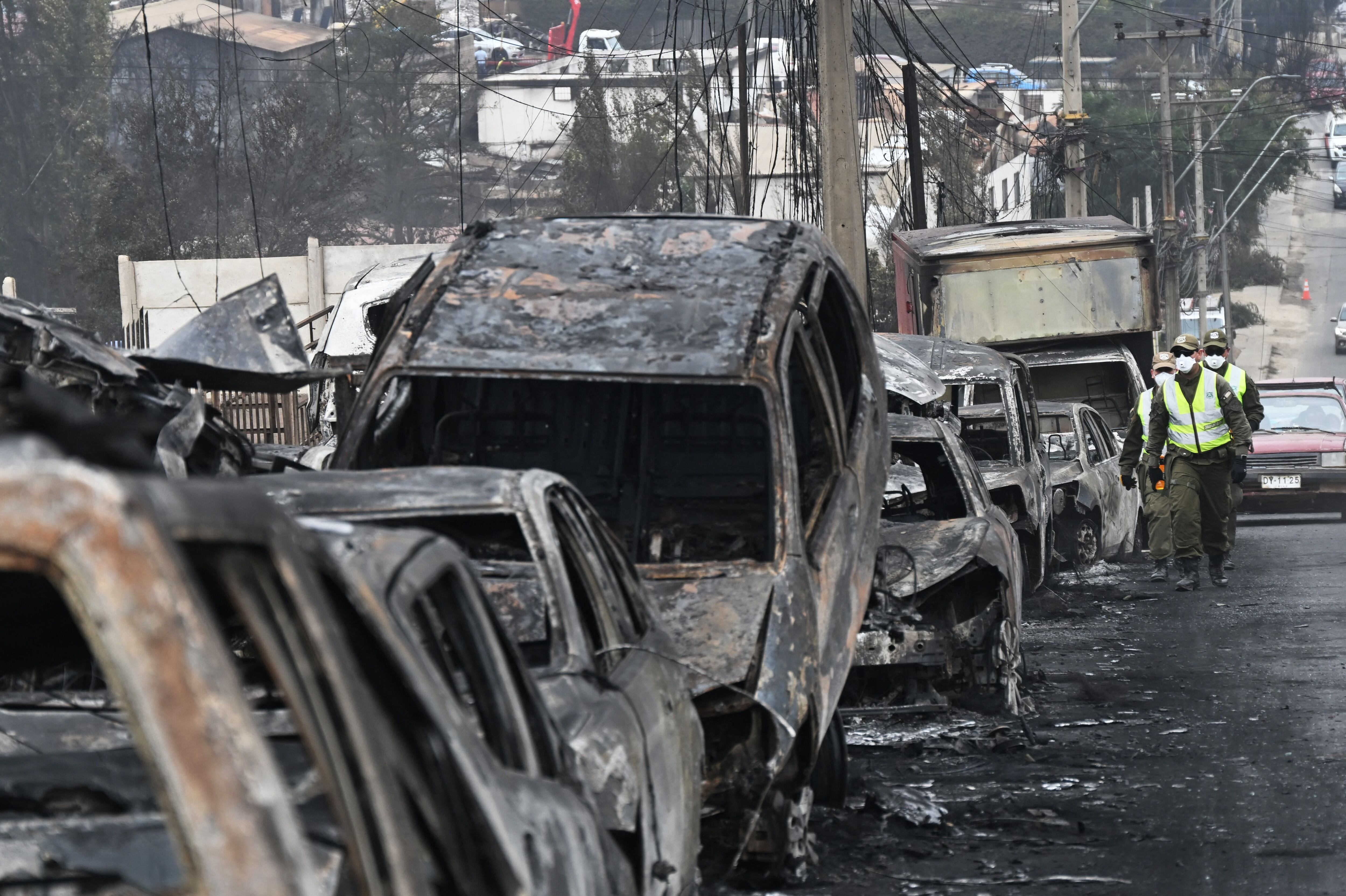 Chilean police walk past burned-out vehicles after a forest fire in Quilpue, Viña del Mar, Chile, on February 4, 2024. (Photo by RODRIGO ARANGUA/AFP).