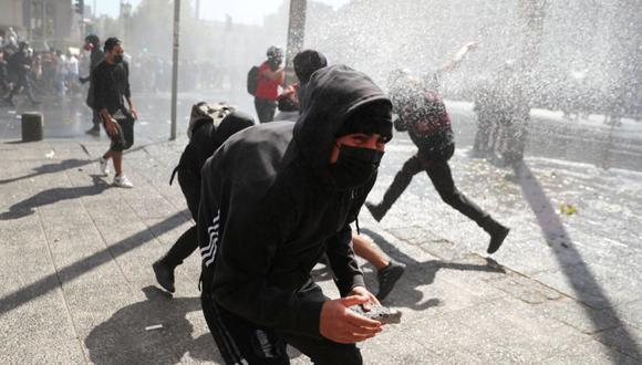 Los manifestantes se cubren mientras un vehículo de la policía antidisturbios rocía agua durante una marcha de protesta estudiantil exigiendo que el gobierno aumente las becas, en Santiago de Chile. (Foto: REUTERS/Ivan Alvarado).