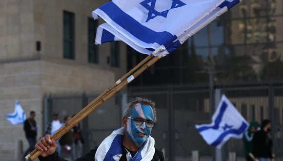 Un manifestante ondea la bandera israelí durante una reunión frente al parlamento de Israel en Jerusalén el 27 de marzo de 2023, en medio de manifestaciones en curso y llama a una huelga general contra el controvertido impulso del gobierno de extrema derecha para reformar el sistema de justicia. (Foto de AHMAD GHARABLI / AFP)