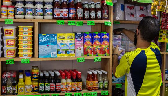 Un empleado de una tienda organiza productos alimenticios en un estante con los carteles de precios de los productos en bolívares en Caracas, Venezuela el 28 de septiembre de 2021. (Foto: CRISTIAN HERNANDEZ / AFP)