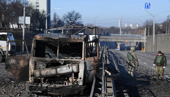 Soldados de Ucrania pasan frente a un vehículo del ejército ucraniano quemado en el lado oeste de Kiev, el 26 de febrero de 2022. (Daniel LEAL / AFP).