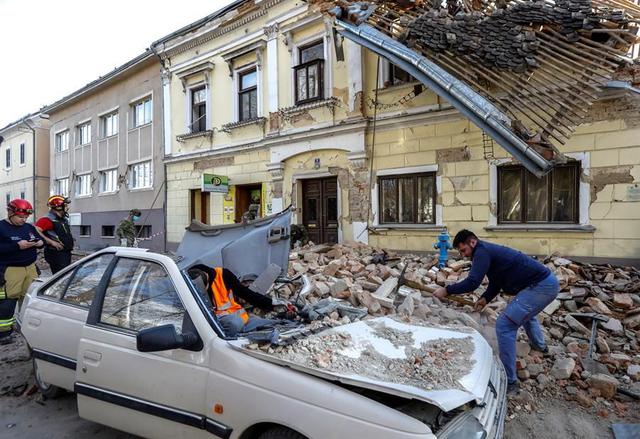 Civiles y soldados limpian los escombros junto a automóviles y edificios dañados por un terremoto en Petrinja, Croacia. (EFE / EPA / ANTONIO BAT).