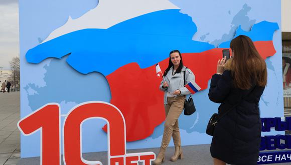 Una mujer posa para fotografías con una decoración artística que muestra el mapa de Crimea con los colores de la bandera tricolor rusa días antes del décimo aniversario de la anexión de Crimea por Rusia, en Simferopol el 13 de marzo de 2024. (Foto de STRINGER / AFP)