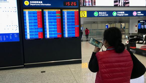 Una mujer china mira la pantalla en el aeropuerto de Wuhan, con la mayoría de vuelos cancelados, poco antes de que se decidiera el cierre temporal del terminal (AFP)