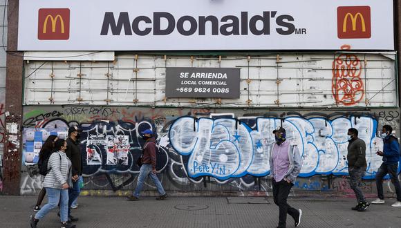 Un grupo de personas camina frente a un antiguo local de comida rápida, tapiado y abandonado desde las protestas que sacudieron Chile en octubre de 2019. (EFE/ Alberto Valdes).