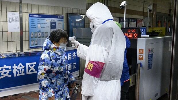 Un empleado de seguridad mide la temperatura corporal de una pasajera a la entrada a una estación de metro en Pekín (Foto: AFP)