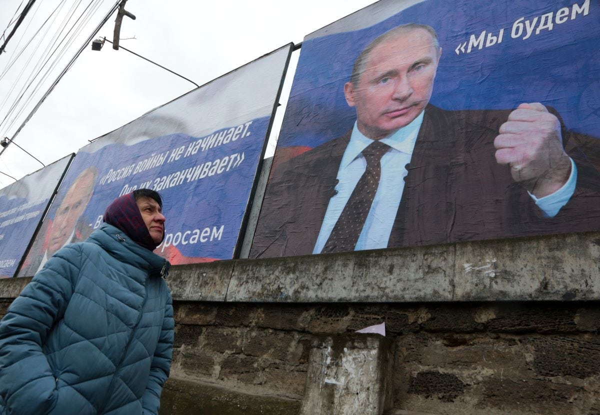 A woman walks past huge banners bearing images of Russian President Vladimir Putin, which read 