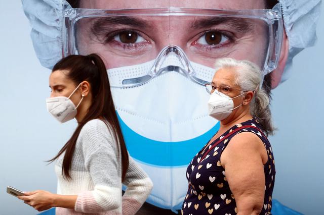 Personas, con máscaras protectoras por el coronavirus, pasan junto a un anuncio de una clínica dental en el barrio de Vallecas en Madrid, España. (REUTERS/Sergio Peréz).