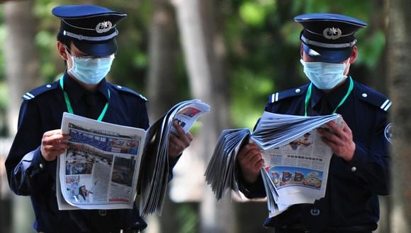 Guardias de seguridad con máscaras faciales leen periódicos mientras están de servicio en el Hotel Guomen en Beijing. (Foto: FREDERIC J. BROWN / AFP)