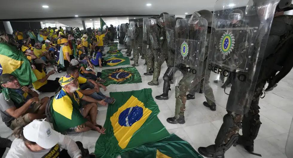 Simpatizantes del expresidente de Brasil, Jair Bolsonaro, se sientan frente a la policía después de ingresar al Palacio de Planalto en Brasilia, el domingo 8 de enero de 2023. (Foto AP/Eraldo Peres).