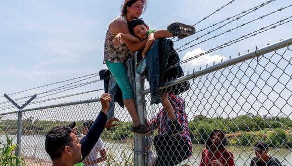 Migrantes trepan una valla de alambre de púas después de cruzar el Río Bravo hacia Estados Unidos desde México, en Eagle Pass, Texas, el 25 de agosto de 2023. (Foto de SUZANNE CORDEIRO / AFP)