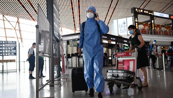 Un hombre que usa un traje protector camina en el aeropuerto internacional de Beijing. Los aeropuertos de Beijing cancelaron más de 1.200 vuelos y las escuelas en la capital china cerraron nuevamente debido a un brote de coronavirus. (Foto por STR / AFP).