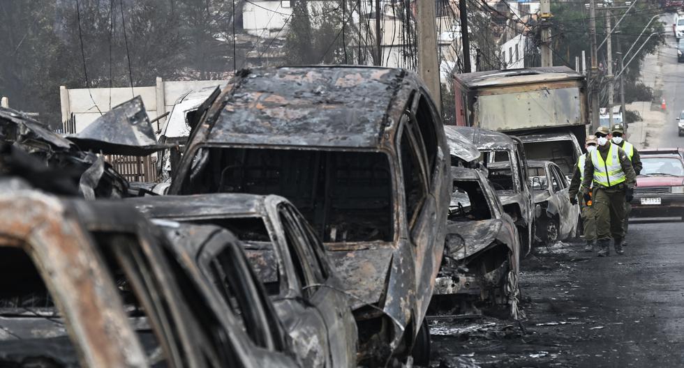 Carabineros chilenos pasan junto a vehículos quemados después de un incendio forestal en Quilpue, Viña del Mar, Chile, el 4 de febrero de 2024. (Foto de RODRIGO ARANGUA/AFP).