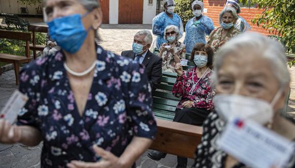 Residentes posan para una foto con sus tarjetas de vacunación junto al ministro de Salud de Chile, Enrique Paris, luego de ser inoculadas con su segunda dosis de la vacuna Sinovac para el coronavirus COVID-19, en el patio de una casa de ancianos en Santiago de Chile. (Foto AP/Esteban Félix).