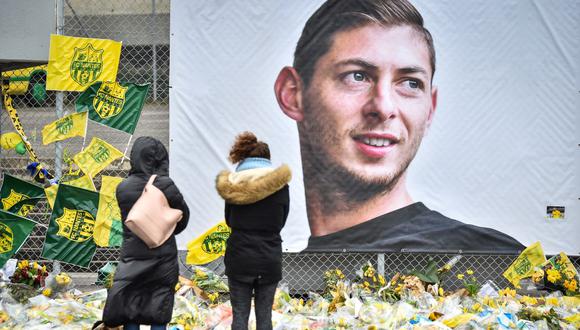 Dos mujeres miran las flores amarillas que están frente al retrato del delantero argentino Emiliano Sala en el estadio Beaujoire en Nantes, el 8 de febrero de 2019. (LOIC VENANCE / AFP).