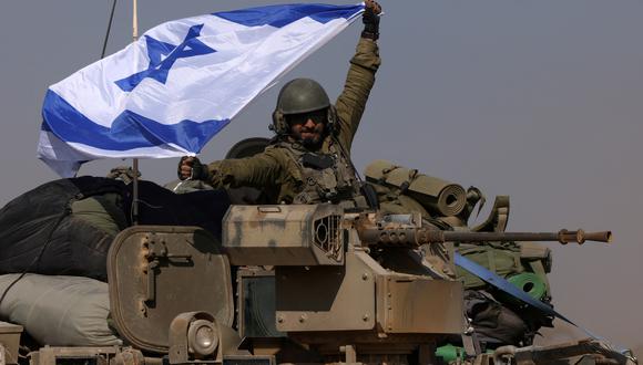 Fotografía tomada cerca de la frontera con la Franja de Gaza muestra a un soldado israelí en un vehículo blindado de transporte de personal (APC) ondeando una bandera israelí mientras las tropas retroceden de la Franja de Gaza, el 31 de diciembre de 2023, en medio de continuas batallas entre Israel y el grupo militante Hamás. . (Menahem KAHANA / AFP)