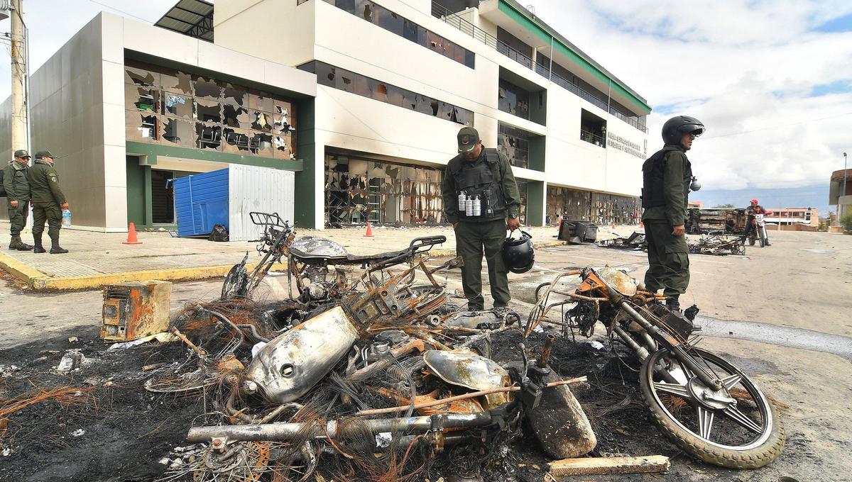 Policías bolivianos observan los destrozos provocados por grupos enardecidos que incendiaron una estación policial en Cochabamba. (EFE/Jorge Abrego).