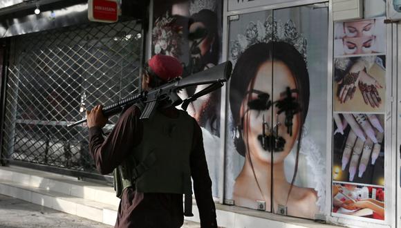 Un combatiente talibán pasa frente a un salón de belleza con imágenes de mujeres desfiguradas con pintura en aerosol en Shar-e-Naw, Kabul, el 18 de agosto de 2021. (Wakil KOHSAR / AFP).