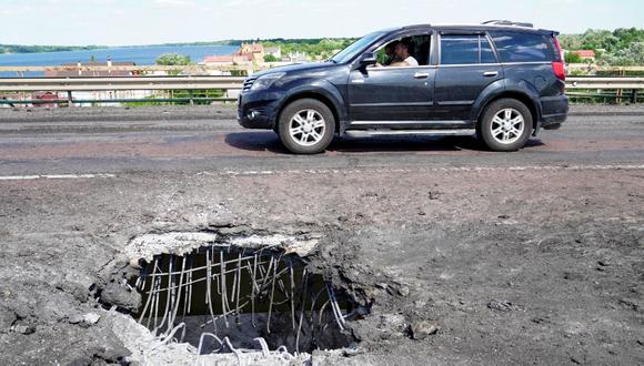 En esta foto de archivo tomada el 21 de julio de 2022, un automóvil pasa junto a un agujero en el puente Antonovsky de Jersón, causado por un ataque con cohetes ucranianos. (Foto: STRINGER / AFP)