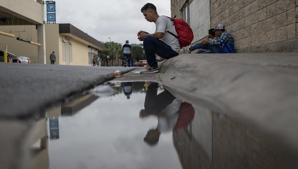 Un migrante que llegó el día anterior desde México pela una naranja mientras espera transporte en una acera en Brownsville, Texas, el 10 de mayo de 2023. (Foto de ANDREW CABALLERO-REYNOLDS / AFP)