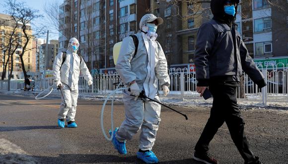 Imagen referencial. Un grupo de trabajadores usan trajes protectores mientras caminan con un residente por la calle, después de desinfectar un área residencial en Beijing, China. EFE