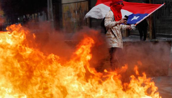 Un manifestante agita una bandera nacional chilena mientras está de pie detrás de un bloqueo en llamas durante las protestas contra el gobierno de Chile. La imagen es del 25 de octubre. (Foto: Reuters)