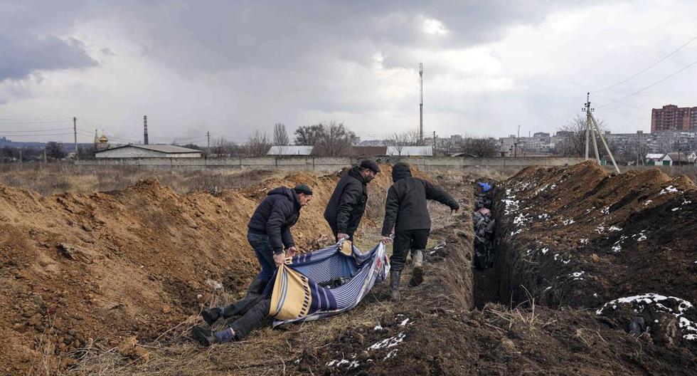 Tres individuos arrastran cadáveres para ser depositados en una larga fosa común en las afueras de Mariúpol (Ucrania) el 9 de marzo del 2022. (AP Photo/Evgeniy Maloletka).