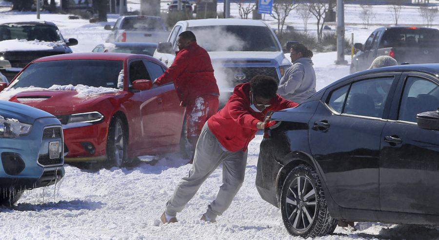 La gente empuja un automóvil libre después de girar en la nieve en Waco, Texas.  (Jerry Larson/Waco Tribune-Herald via AP)