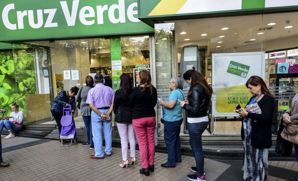 Un grupo de personas hace cola ante una farmacia de santiago. (Photo by MARTIN BERNETTI / AFP).