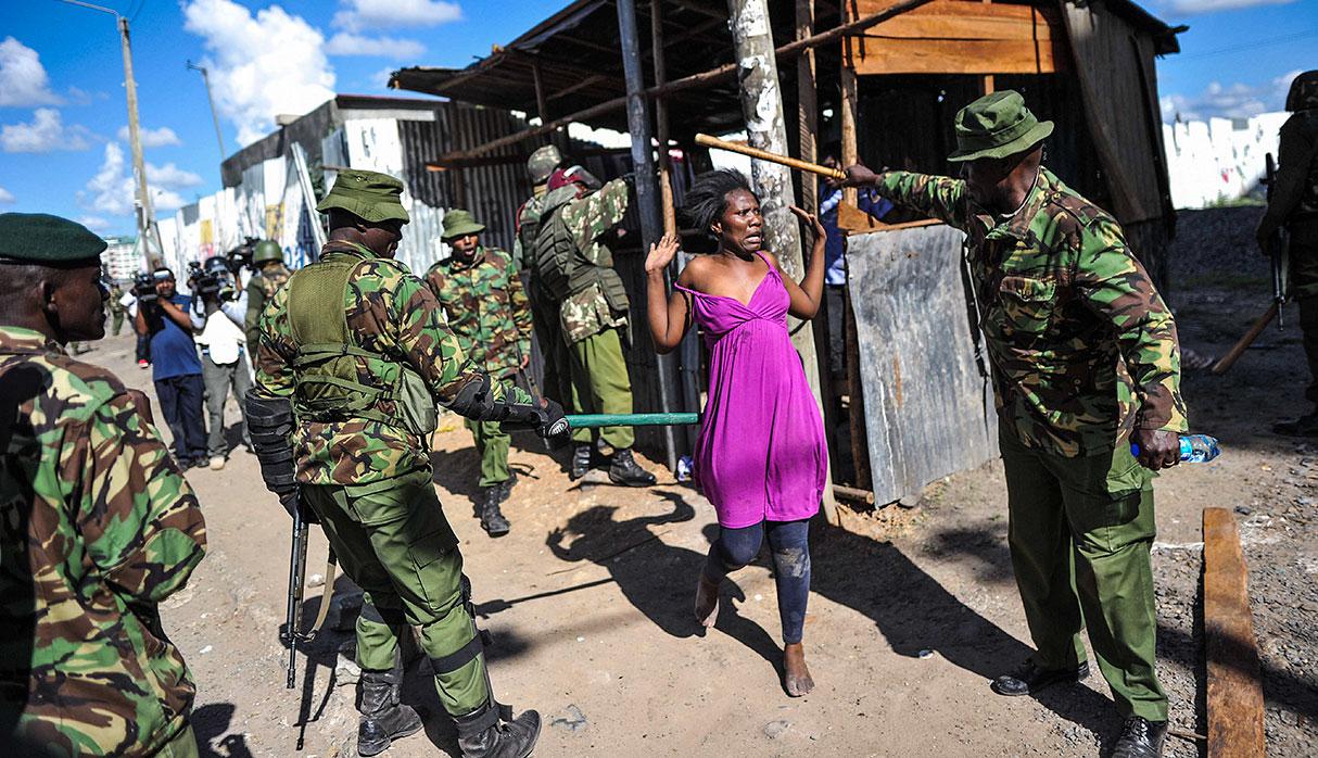 TOPSHOT - A woman puts her hands up as anti-riot policemen flush out opposition supporters, who had taken cover in a shack to escape teargas, during demonstrations in the Umoja subururb of Nairobi on November 28, 2017, following a denial of permission by police to the National Super Alliance (NASA) leader to hold a rally concurrently to the inauguration of the country's new president. President Uhuru Kenyatta vowed to be the leader of all Kenyans and work to unite the country after a bruising and drawn out election process that ended with his swearing-in. / AFP / TONY KARUMBA
