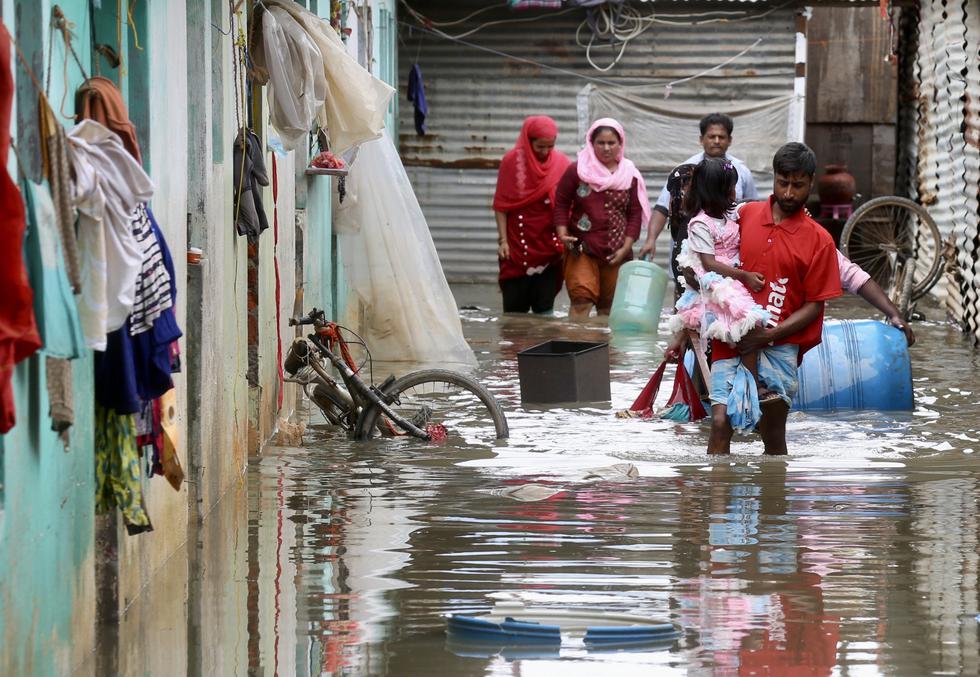 Personas con sus objetos de valor mientras caminan por una carretera inundada tras una fuerte lluvia en Bangalore, India. EFE/EPA/JAGADEESH NV