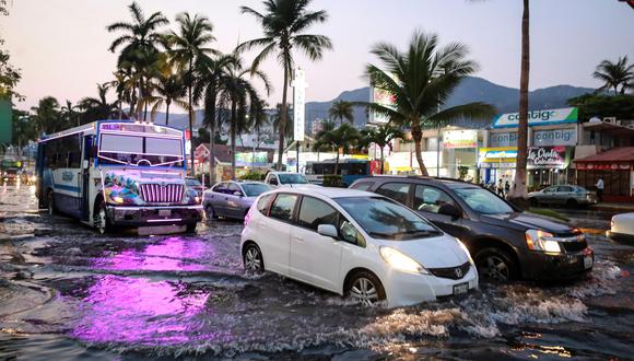 Varios vehículos transitan por una calle inundada debido a las fuertes lluvias del pasado lunes, en Acapulco.