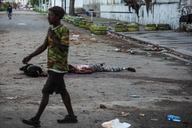 Un hombre pasa frente a dos cadáveres este domingo en una calle de Puerto Príncipe, capital de Haití. (EFE/ Johnson Sabin).