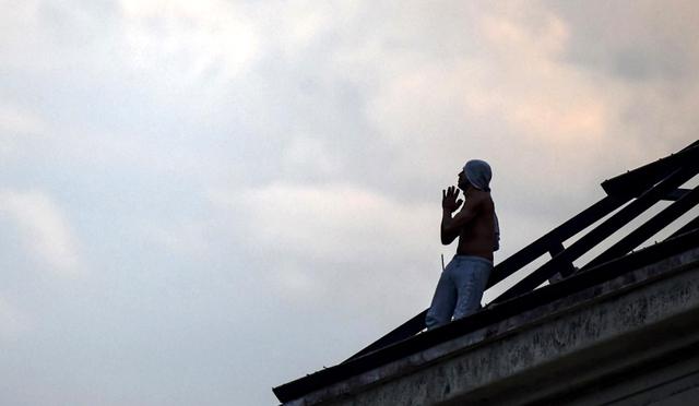 Un recluso hace un gesto mientras se sienta en un techo destruido de la prisión de Villa Devoto durante un motín en demanda de medidas preventivas contra la propagación de COVID-19, en Buenos Aires. (Foto: AFP/Ronaldo SCHEMIDT)