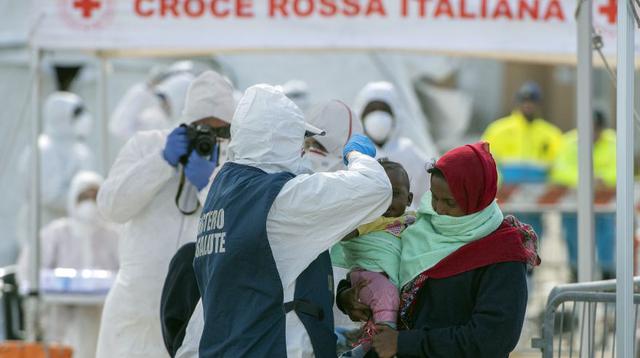 Funcionarios italianos con trajes especiales controlan a los migrantes que desembarcan del barco Sea Watch. (AFP).