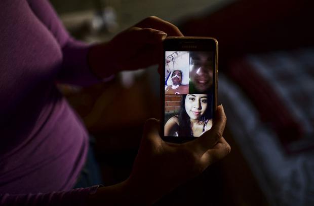 Priscila Almirón muestra una imagen de una videollamada familiar en su teléfono móvil mientras su padre estaba hospitalizado. (Foto de RONALDO SCHEMIDT / AFP).