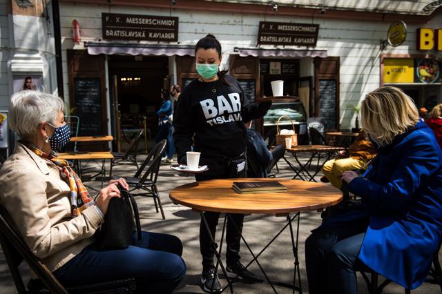Una camarera con una máscara facial sirve a los clientes en la terraza de un café en Bratislava, Eslovaquia, el pasado 6 de mayo, en medio de la pandemia del nuevo coronavirus COVID-19. El gobierno eslovaco está aliviando las restricciones debido al bajo número de nuevas infecciones por coronavirus. (VLADIMIR SIMICEK / AFP)