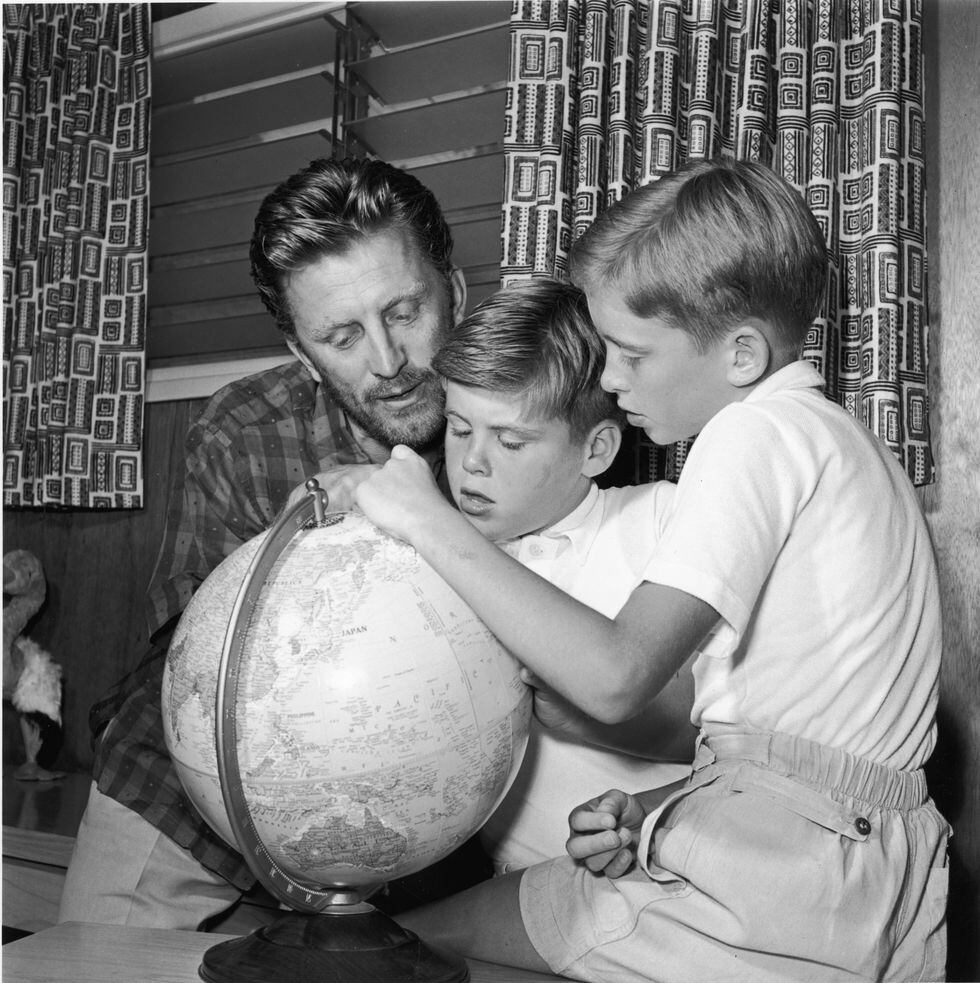 1956. El actor estadounidense Kirk Douglas observa un globo terráqueo con dos de sus hijos, Joel (centro) y Michael Douglas. [Foto: Getty Images]