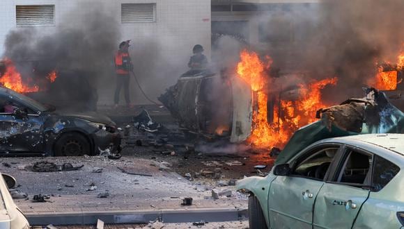 La gente intenta extinguir el fuego de los automóviles tras un ataque con cohetes desde la Franja de Gaza hacia Ashkelon, sur de Israel, el 7 de octubre de 2023. (Foto de AHMAD GHARABLI / AFP).