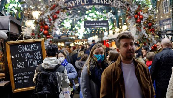 Los compradores, algunos de los cuales se cubren la cara para combatir la propagación del Covid-19, pasan por puestos y tiendas en el Apple Market en Covent Garden el último sábado para ir de compras antes de Navidad, en el centro de Londres. (Foto: Tolga Akmen / AFP)