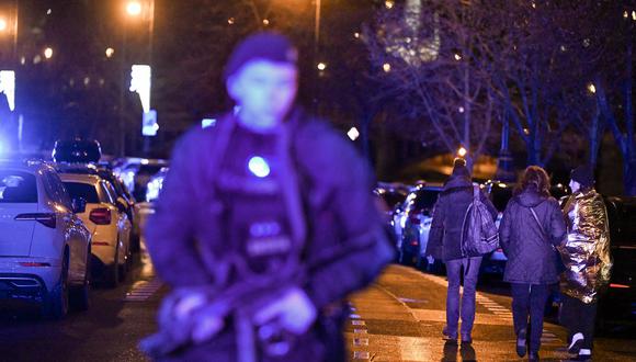 Personas atrapadas en un tiroteo pasan junto a un policía armado cerca de la Universidad Carolina en el centro de Praga, el 21 de diciembre de 2023. (Foto de Michal CIZEK / AFP)