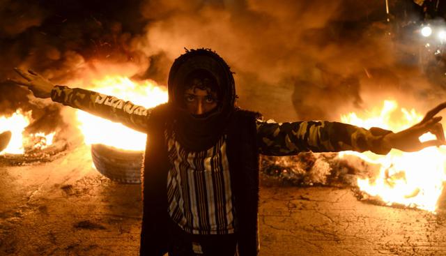 Un enmascarado protestante sale entre el fuego mientras realiza un gesto de victoria. (AFP).