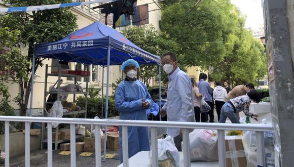 Trabajadores con máscaras faciales parados cerca de un área de recogida de paquetes en un barrio de Shanghái, China.