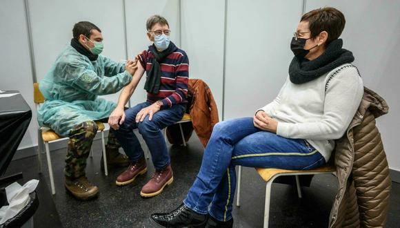 Un soldado suizo administra una vacuna de refuerzo contra el COVID-19 a un hombre junto a su esposa en Delemont, en el norte de Suiza, el 14 de diciembre de 2021. (Foto: Fabrice COFFRINI/ AFP)