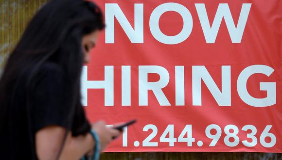 Una mujer camina junto a un cartel que dice "Ahora contratando" afuera de una tienda el 16 de agosto de 2021 en Arlington, Estados Unidos. (Olivier DOULIERY / AFP).