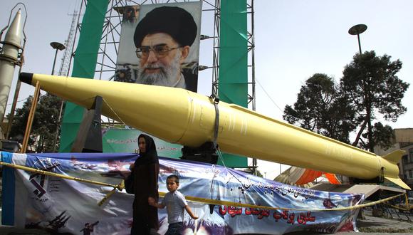 Una mujer iraní y su hijo pasan junto a los misiles Shahab-2 y Shahab-3 en exhibición frente a un gran retrato del líder supremo de Irán, el ayatola Alí Jamenei. (ATTA KENARE / AFP).